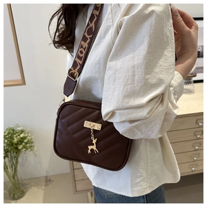 Close-up of dark brown quilted leather crossbody bag with deer charm and wide patterned strap
