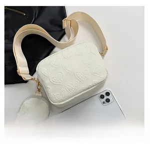 Detail of cream canvas square bag with embossed heart pattern and mini round pouch charm
