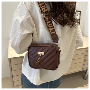 Close-up of brown quilted leather crossbody bag with deer pendant and wide strap
