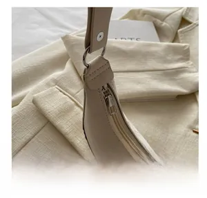 Detail view of smooth metal zipper and silver hardware on beige crescent underarm bag