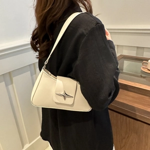 Chic beige underarm baguette bag with silver star buckle worn by a model in a cafe