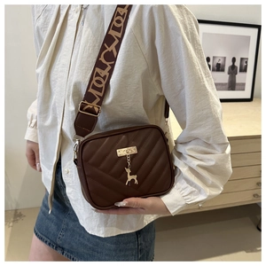 Detail of coffee crossbody bag featuring V-quilted faux leather and a gold elk pendant