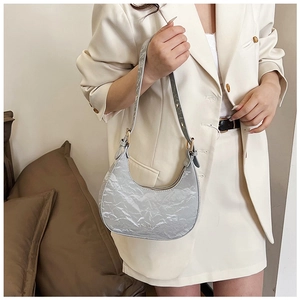 Silver crescent shoulder bag with pleated metallic texture on a cream-colored blazer