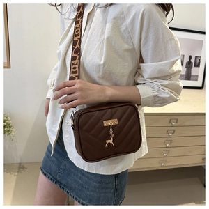 Detail of V-quilted brown crossbody bag with gold deer charm and patterned strap