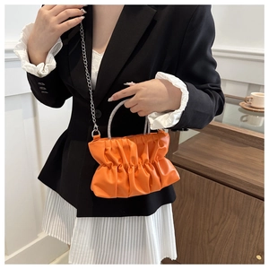 Detail of orange pleated cloud bag featuring rhinestone handle and silver chain strap