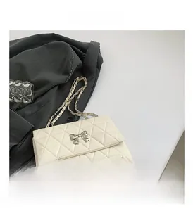 Detail of cream quilted PU crossbody bag with silver bow accent and leather chain strap