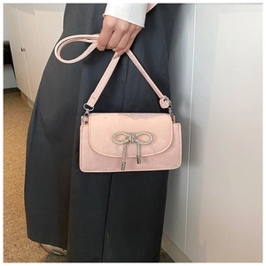 Detail of light pink suede square bag featuring a silver bow pendant and adjustable strap