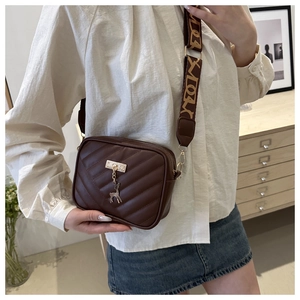 Detail of brown quilted crossbody bag with wide printed strap and deer charm on white shirt