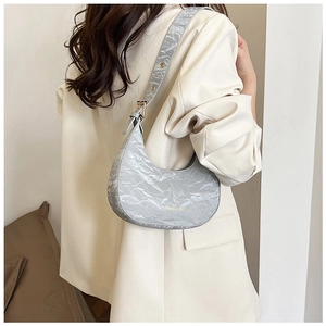 Detail of silver crescent bag featuring metallic crinkle texture and gold logo lettering