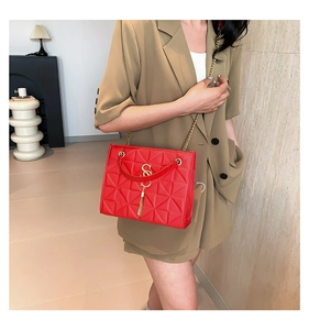 Detail of red geometric quilted chain bag with gold tassel on a model wearing khaki blazer