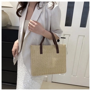 Close-up of beige herringbone weave texture and brown handle on woven tote bag