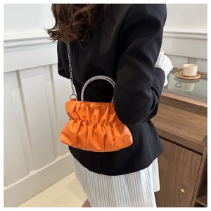 Detail of orange pleated crossbody bag featuring a rhinestone handle and silver chain
