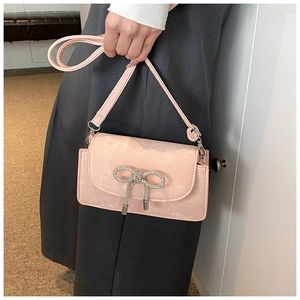 Pink suede crossbody bag with sparkling rhinestone bow pendant detail held by a model