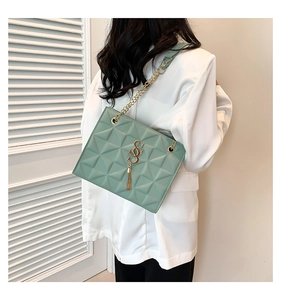 Detail of green quilted shoulder bag with gold S-pendant and metal fringe