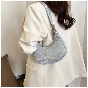 Detail of silver crescent moon shoulder bag with metallic crinkled texture and gold buckle