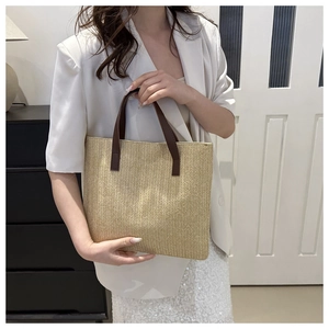 Detail view of woven tote bag with brown leather handles and natural textured pattern