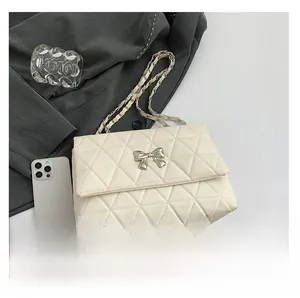 Detail of cream quilted shoulder bag with silver bow accent and chain strap