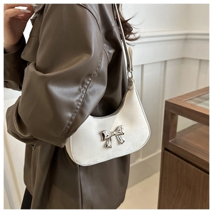 Detail of a beige half-moon shoulder bag with a silver metal bow buckle decoration
