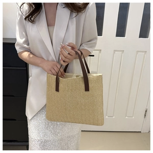 Detail of woven straw tote bag with brown leather handles and magnetic snap closure