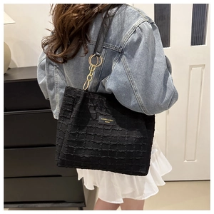 Detail of black textured tote bag with gold chain strap and fashion brand logo