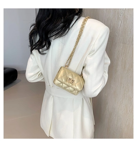 Detail of a mini gold quilted chain bag with a metallic finish and square lock clasp
