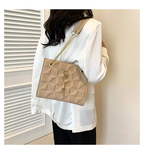 Detail of beige quilted shoulder bag with gold chain strap and elegant metal tassel charm