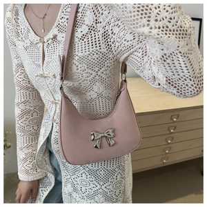 Close-up of a pink patent leather baguette bag with a silver metal bow accent