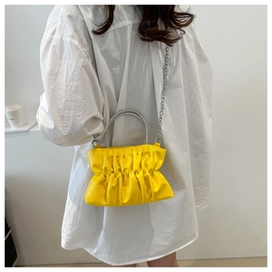 Detail of yellow pleated cloud bag with silver rhinestone handle and chain strap on model