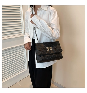 Detailed close-up of black quilted shoulder bag with gold bow lock and chain strap