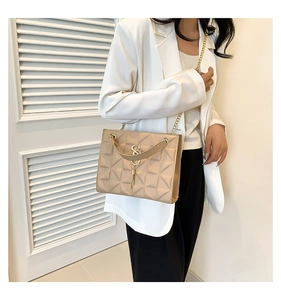Close-up of beige quilted shoulder bag featuring gold S-buckle and elegant chain strap