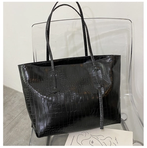 Détail d'un cabas noir à motif crocodile avec gland en cuir sur chaise acrylique