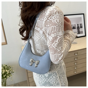 Detail of light blue hobo bag with silver bow ornament worn with white crochet top
