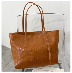 Détail d'un sac cabas marron caramel à motif crocodile sur une chaise acrylique