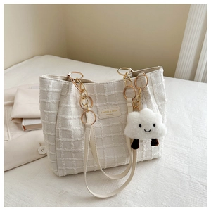 Close-up of white tweed tote bag with gold chain strap and fluffy cloud pendant