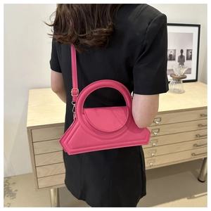 Borsa a mano geometrica rosa vivace con manico rotondo sopra un mobile