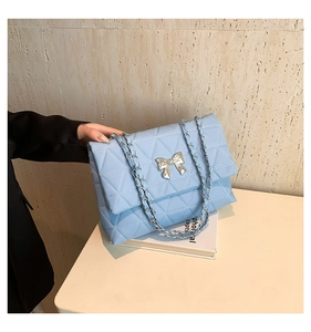 Détail d'un sac à main bleu matelassé avec nœud argenté et bandoulière en chaîne métal