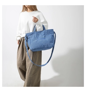 Blue corduroy tote bag detail showing FASHION embroidery and crossbody strap on model