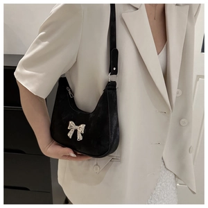 Close-up of black matte baguette bag with silver metal bow detail on beige blazer
