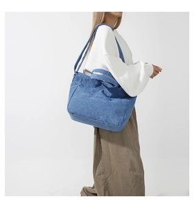 Detail of blue corduroy tote bag with Fashion embroidery on a side-carrying model