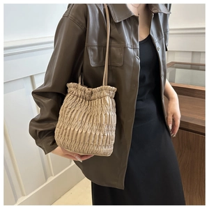 Detailed side view of beige pleated drawstring bucket bag worn by model in a soft studio light