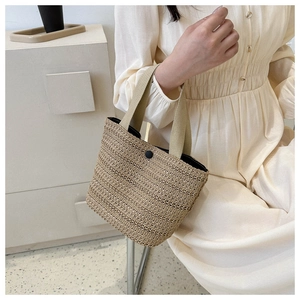 Detail of hand-woven straw tote bag with black button closure and beige handles