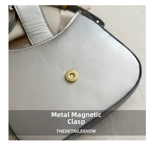 Gros plan du fermoir magnétique doré sur un sac à main gris argenté à texture fine