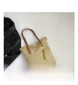 Detail of woven straw tote bag with brown leather handles and gold tassel charm decor