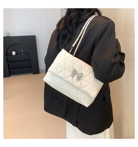 Detail of white quilted shoulder bag with silver bow and leather chain strap on a model