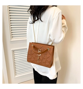 Detail of caramel brown quilted handbag with metal S logo and chain strap on model