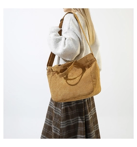 Model wearing a mustard yellow corduroy large shoulder bag with embroidered brand logo