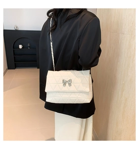 Detail of cream quilted shoulder bag with silver bow accent and metal chain strap