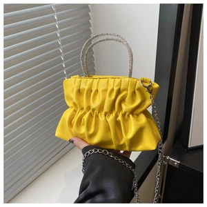 Detail of yellow cloud pleated handbag with rhinestone handles and silver chain strap