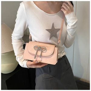 Detail of pink bow handbag in shiny patent leather worn by a model in a cozy interior
