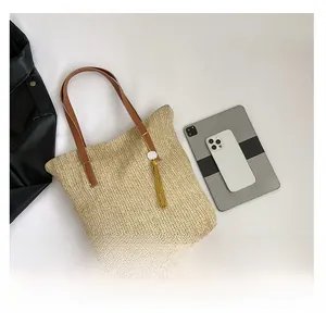 Macro detail of beige woven tote bag with brown leather straps and elegant tassel charm